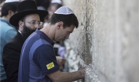 Lionel Messi (kanan), pemain bintang Barcelona, meletakkan kertas berisi harapan di sela 'Tembok Ratapan', Jerusalem, Israel, Ahad (4/8). 