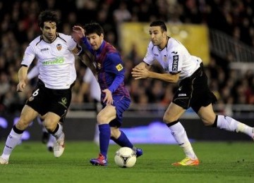 Penyerang Barcelona, Lionel Messi diapit dua pemain bertahan Valencia ...