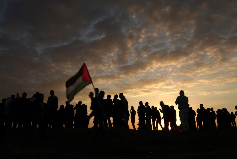 Pengunjuk rasa melambaikan bendera Palestina saat terjadi bentrokan di dekat perbatasan dengan Israel di timur Kota Gaza, Jumat (15/12). Demonstran memprotes keputusan Presiden AS Donald Trump mengakui Yerusalem sebagai Ibu Kota Israel. 