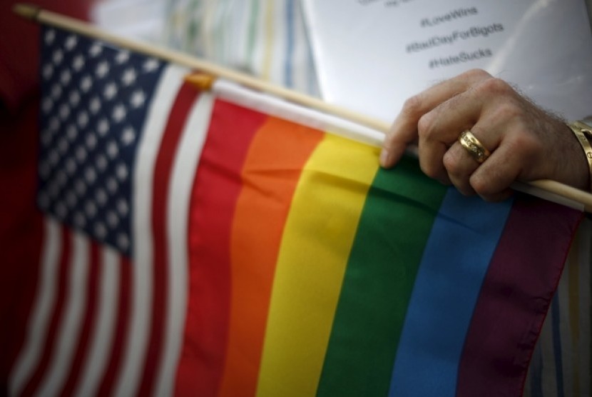 Seorang pria menggenggam bendera AS dan bendera pelangi, yang menjadi simbol kaum LGBT, menyusul keputusan dilegalkan perkawinan sejenis di seluruh AS.