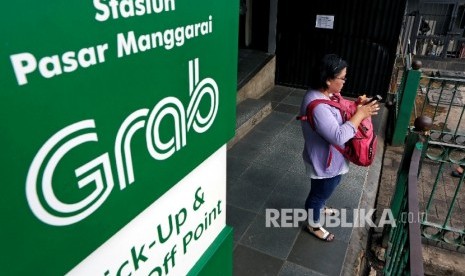 [ilustrasi] Seorang wanita sedang mengecek ponselnya di sebelah banner iklan Grab di Stasiun Manggarai, Jakarta. Grab Holdings berencana membentuk dana abadi GrabForGood.