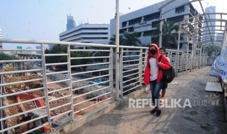 Warga melintasi Jembatan Penyeberangan Orang (JPO) yang terdampak pembangunan LRT di kawasan Kuningan, Jakarta Selatan, Ahad (22/7).