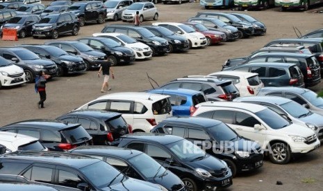 Warga melintas didekat mobil yang terparkir di Park and Ride Jalan MH Thamrin, Jakarta.