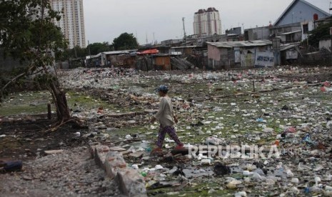 Warga melintasi diantara tumpukan sampah di pemukiman penduduk Kawasan Muara Baru, Jakarta, Kamis (28/12).