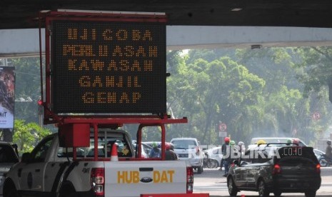 Kendaraan melintas di dekat papan sosialisasi uji coba perluasan ganjil genap di kawasan Pancoran, Jakarta Selatan, Senin (2/7).