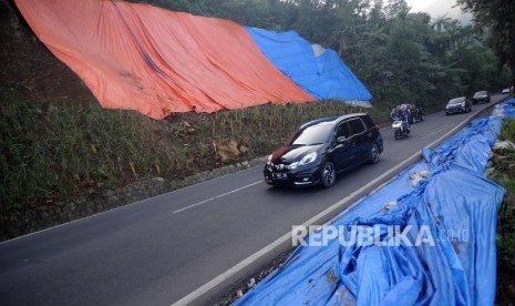 Kendaraan melintas di dekat bekas longsoran tebing yang ditutupi terpal di kawasan Puncak, Bogor, Jawa Barat, Sabtu (9/6).