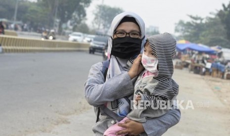 Seorang warga menggendong anaknya menggunakan masker di Jalan Soekarno Hatta, Pekanbaru, Riau, Selasa (17/9).