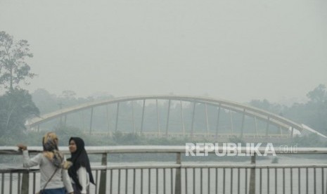 Warga beraktivitas dengan latar belakang aliran Sungai Siak yang diselimuti asap kebakaran lahan gambut di Alun-alun Kabupaten Siak, Riau, Kamis (12/9).