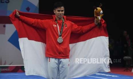 Atlet Wushu Indonesia Edgar Xavier Marvelo  menggunakan bendera merah putih  usai  prosesi penyerahan medali cabang olahraga Wushu Changquan Putra di Hall B, JIE Expo Kemayoran, Jakarta, Ahad (19/8).