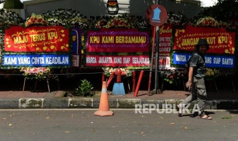 Warga melintas di dekat karangan bunga yang terpasang di depan Gedung Komisi Pemilihan Umum (KPU), Jakarta, Ahad (21/4).