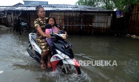 Warga melintasi genangan air saat terjadi banjir rob di kawasan Muara Angke, Jakarta Utara, Selasa (22/1).