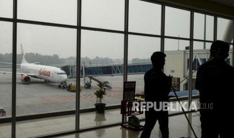 Penumpang melintas dengan latar belakang pesawat yang diselimuti kabut asap di Bandara Sultan Syarif Kasim II Pekanbaru, Riau, Sabtu (21/9).