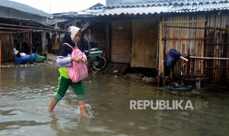 Anak-anak melintasi genangan air saat terjadi banjir rob di kawasan Muara Angke, Jakarta Utara, Selasa (22/1).