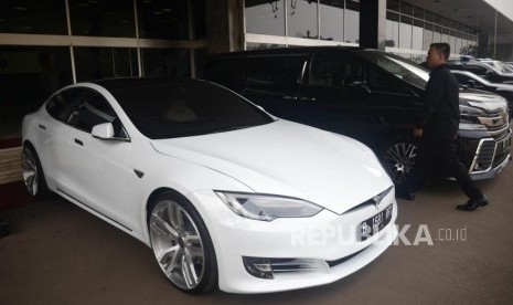 Seorang melintas didekat mobil listrik Tesla yang terparkir di depan Gedung Nusantara III, Kompleks Parlemen, Jakarta, Selasa (3/7).