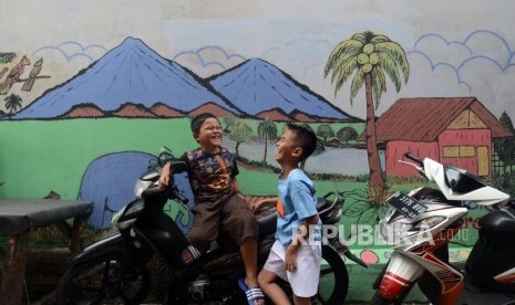 Anak-anak bermain di dekat tembok yang dihiasi mural di kawasan Jembatan Lima, Tambora, Jakarta Barat.