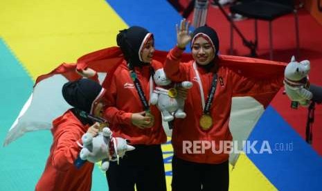 Pesilat Indonesia Pramuditya Yuristya, Lutfi Nurhasanah dan Gina Tri Lestari membentangkan bendera merah putih usai pertandingan cabang olahraga silat Asian Games 2018 kategori regu putri di Padepokan Pencak Silat TMII, Jakarta, Rabu (29/8).