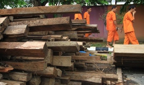 Sejumlah tersangka berjalan melewati barang bukti kayu hasil pembalakan liar, di Kota Pekanbaru, Kamis (11/10).