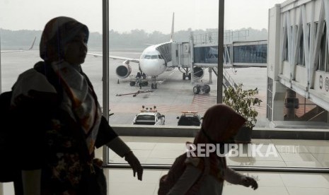 Penumpang melintas dengan latar belakang pesawat di Bandara Sultan Syarif Kasim II Pekanbaru, Riau. 