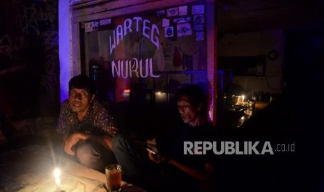 Warga menikmati minuman di warung nasi ketika terjadinya pemadaman listik di kawasan padat penduduk Karet Tengsin, Jakarta, Ahad (4/8).