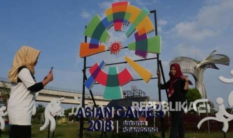 Dua  remaja saling berswa foto di depan logo Asian Games yang terletak di bundaran komplek Jakabaring Sport City, Palembang, Jumat (3/8).