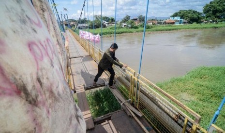 Warga menyeberangi Sungai Citarum menggunakan jembatan gantung yang rusak di Rancamanyar, Kabupaten Bandung, Jawa Barat, Minggu (30/12/2018).