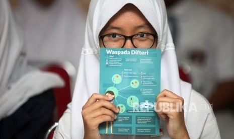 Seorang siswi memperlihatkan brosur waspada difteri seusai melakukan imunisasi difteri saat sosialisasi komitmen pelaksaan kegiatan Outbreak Response Immunization (ORI) Difteri di Sekolah SMAN 33 Jakarta, Jalan Kamal Raya, Jakarta Barat, Senin (11/12).