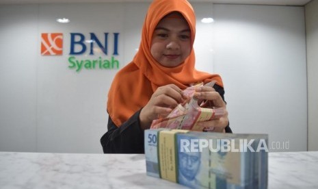 Karyawan mengitung uang nasabah di kantor layanan BNI Syariah, Jakarta, Senin (5/11).