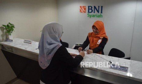 Karyawan melayani transaksi nasabah di kantor layanan BNI Syariah, Jakarta, Senin (5/11).