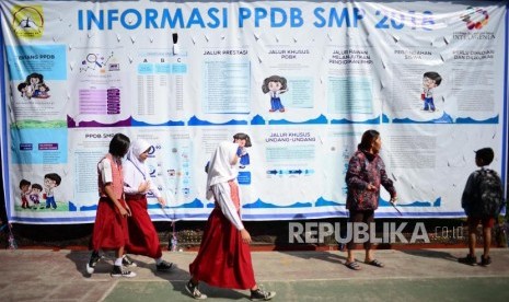 PPDB Kota Bandung. Siswa berseragam sekolah dasar melintasi baliho informasi Perimaan Peserta Didik Baru (PPDB) di SMPN 34 Bandung, Senin (2/7).