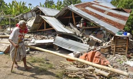 Warga berjalan di depan rumah yang roboh akibat gempa di Desa Sajang, Kecamatan Sembalun, Selong, Lombok Timur, NTB, Minggu (29/7).