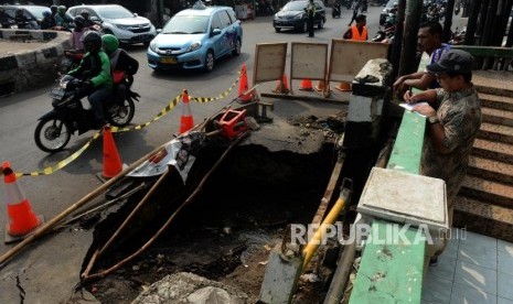 Pengendara motor melintas di dekat jalan yang amblas di Jalan Raya Sawangan, Depok, Jawa Barat, Jumat (28/6).