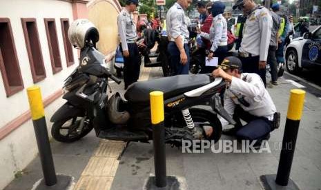 Petugas mengembosi kendaraan bermotor yang parkir di badan jalan ketika melakukan razia parkir liar di kawasan Kramat Raya, Jakarta Pusat, Kamis (30/8).