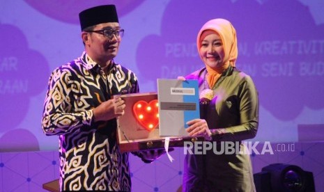 Gubernur Jabar Ridwan Kamil memberikan buku modul Sekolah Perempuan Capai Impian dan Cita-cita (Sekoper Cinta) kepada istrinya yang juga Ketua Penggerak PKK Jabar Atalia Praratya pada Festival Kabupaten/Kota Layak Anak (KLA) dan Expo UKM Perempuan dalam rangka Hari Ibu (PHI) ke-90, di Gedung Sabuga, Kota Bandung, Ahad (16/12).