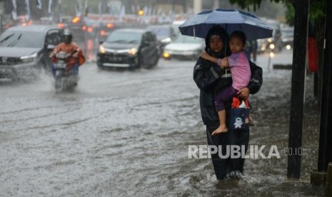 Warga melintasi genangan air saat terjadi banjir di kawasan Pancoran, Jakarta, Selasa (18/12).