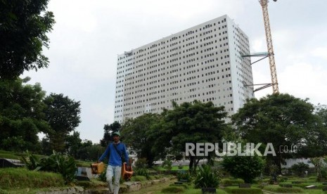 Pekerja melintasi pemakaman dengan latar belakang proyek pembangunan Rumah Susun Milik (Rusunami) Klapa Village di kawasan Pondok Kelapa, Jakarta, Kamis (11/4).