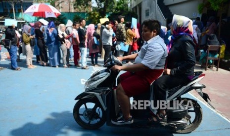 PPDB Kota Bandung. Seorang siswa berseragam sekolah dasar mengendarai sepeda motor melintasi antrean Perimaan Peserta Didik Baru (PPDB) di SMPN 34 Bandung, Senin (2/7).