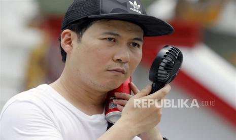  Seorang turis menggunakan kipas genggam untuk mendinginkan diri saat berkunjung ke Wat Arun, atau Kuil Fajar, di Bangkok, Thailand,  Senin (24/4/2023). Pengidap diabetes cenderung mengalami dehidrasi lebih cepat daripada orang lain.