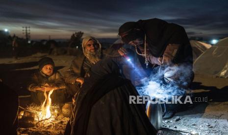 Sebuah keluarga menyiapkan teh di luar kantor Direktorat Bencana tempat mereka berkemah, di Herat, Afghanistan, pada 29 November 2021. Amerika Serikat (AS) mengizinkan bank-bank internasional mentransfer uang ke Afghanistan untuk tujuan kemanusiaan. 