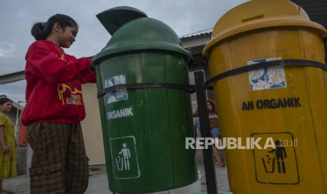 Seorang anak membuang sampah ke dalam tong sampah yang telah dipisahkan antara organik dan anorganik di sebuah rumah.