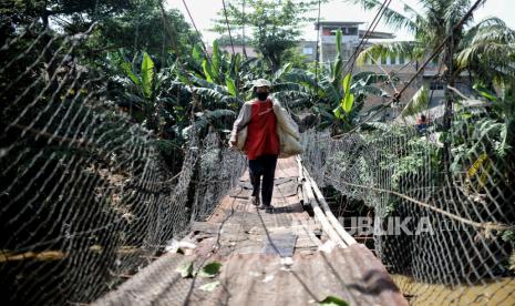 Warga melintasi jembatan gantung Srengseng Sawah yang rusak di Jakarta, Senin (13/12). Jembatan yang merupakan akses penyeberangan  warga dari Depok menuju Jakarta tersebut belum kunjung diperbaiki, pasalnya kontruksi jembatan yang ditopang oleh tali baja dan bambu tersebut nampak tak terawat dan  keropos sehingga dapat membahayakan pejalan kaki saat menyeberang. Sejumlah warga berharap perbaikan jembatan tersebut segera dilakukan untuk memberikan keamanan dan kenyamanan bagi warga. 