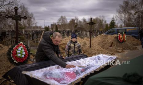 Vova, 10, melihat jenazah ibunya, Maryna, yang terbaring di peti mati saat ayahnya, Ivan Drahun, berdoa saat pemakamannya di Bucha, di pinggiran Kyiv, Ukraina, pada Rabu, 20 April 2022. 