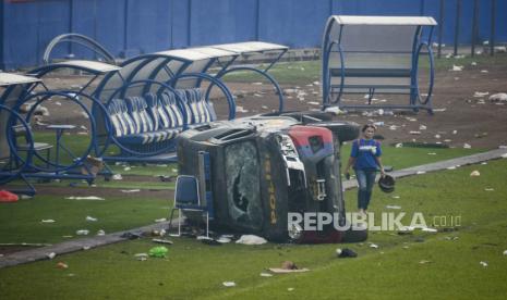  Seorang wanita berjalan melewati kendaraan polisi yang rusak di dalam stadion Kanjuruhan di Malang, Jawa Timur, 02 Oktober 2022. Sedikitnya 127 orang termasuk petugas polisi tewas sebagian besar karena terinjak-injak setelah bentrokan antara penggemar dua tim sepak bola Indonesia, menurut polisi .