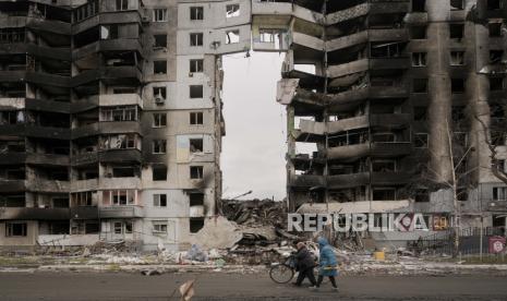 Wanita yang membawa produk makanan berjalan di dekat gedung apartemen yang hancur di Borodyanka, Ukraina, Rabu, 6 April 2022. 