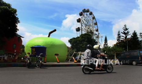 Pengendara motor melintas di depan wahana wisata bianglala yang ditutup saat penerapan Pembatasan Sosial Berskala Besar (PSBB) di Alun-alun Kota Batu, Jawa Timur, Selasa (26/5/2020). Ada sekitar 50 hotel di Kota Batu telah mengajukan izin kembali beroperasi usai PSBB. Ilustrasi. 