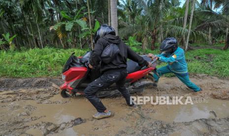 Pengendara mendorong sepeda motornya yang terperosok saat melintasi jalan rusak. (Ilustrasi)