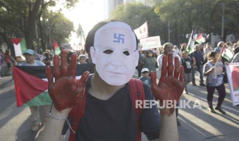 Seorang pria bertopeng wajah Benjamin Netanyahu dan tangan dicat merah melakukan pawai menentang agresu Israel di Gaza, di Mexico City, Ahad, 5 November 2023.