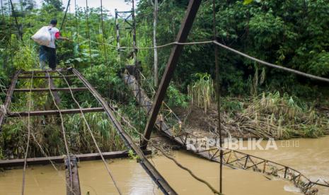 Warga melintasi jembatan gantung lama yang kondisinya telah rusak di Desa Parung Kujang, Lebak, Banten, Senin (14/12/2020). Menurut keterangan warga setempat jembatan yang menghubungkan dua desa tersebut putus pada Minggu (13/12/2020) setelah diterjang oleh luapan Sungai Ciujung dan menyebabkan sembilan warga luka-luka akibat terjatuh dari jembatan. 