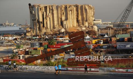  Orang-orang melewati monumen simbol keadilan yang terletak di depan silo gandum yang menjulang tinggi yang hancur dalam ledakan besar Agustus 2020 di pelabuhan Beirut yang merenggut nyawa lebih dari 200 orang, di Beirut, Lebanon, Rabu, 4 Agustus 2021. Setahun setelah ledakan mematikan itu, keluarga para korban disibukkan dengan memenangkan keadilan bagi orang yang mereka cintai dan menghukum elit politik Lebanon, yang disalahkan karena menyebabkan bencana melalui korupsi dan pengabaian mereka.