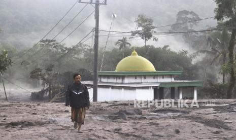 Seorang pria berjalan melewati masjid yang sebagian tertutup abu vulkanik dari letusan Gunung Semeru di desa Kajar Kuning di Lumajang, Jawa Timur, Indonesia, Senin, 5 Desember 2022. Gunung berapi tertinggi di Indonesia di pulau terpadatnya melepaskan awan gas yang membakar dan sungai lava Minggu dalam letusan terbarunya.