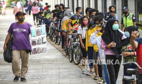 Pedagang menjajakan masker kepada warga yang antre untuk berolahraga di Jakarta International Velodrome, Rawamangun, Jakarta, Ahad (25/10/2020). Jakarta International Velodrome (JIV) kembali dibuka untuk publik selama penerapan Pembatasan Sosial Berskala Besar (PSBB) transisi di ibu kota, namun membatasi jumlah pengunjung sebanyak 1.500 orang atau 50 persen dari kapasitas normal yakni sebanyak 3.000 orang. 